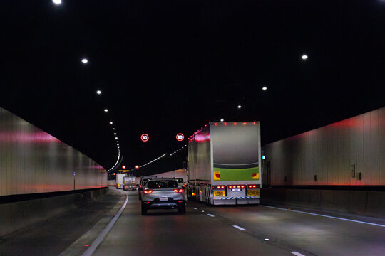 Traffic on road cars and truck driving through tunnel under city with 80 speed limit signs
