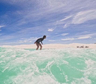 Female woman  surfer riding small waves on longboard  in summer wetsuit on sunny clear day