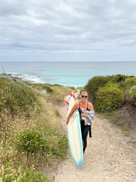 Woman holding mid length surfboard on overcast beach background