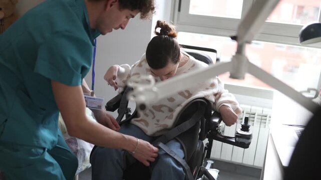 Supportive male caregiver helping a smiling woman with a disability, securing her in a motorized wheelchair at home. Empathy and compassionate assistance from a dedicated healthcare professional