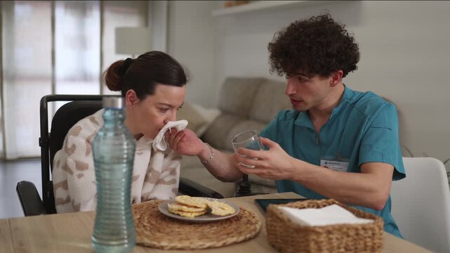 Young male nurse providing immediate first aid to a disabled woman in a wheelchair who is choking while eating breakfast at home, showcasing professional healthcare support and assistance
