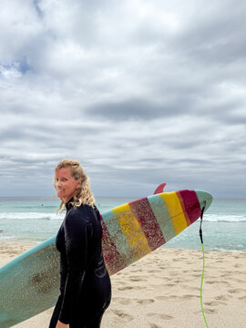 Woman holding mid length surfboard on overcast beach background