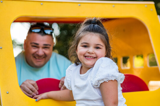 A father and his daughter enjoy their time at a yellow playhouse in the park during the afternoon