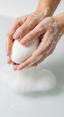 Fototapeta premium Two hands covered with soap bubbles holding a white soap bar, water dripping, representing hygiene, cleanliness, health, or skin care routine