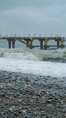 Fototapeta premium Weathered pier over turbulent waves on rocky beach under cloudy sky