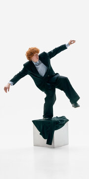 Businessman losing balance on pedestal in formal suit on white studio background. Concept of business instability, market volatility, strategic miscalculation and leadership under pressure.