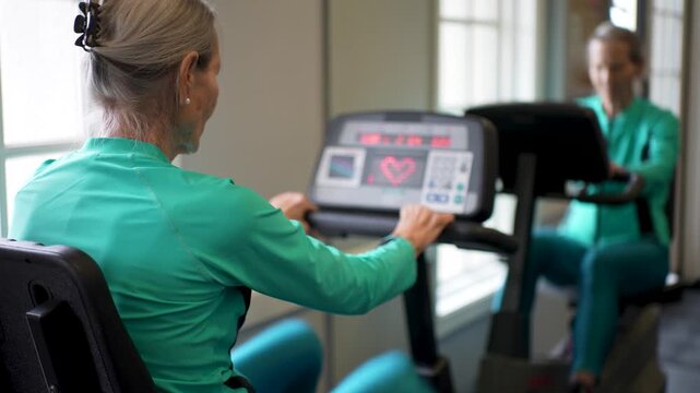 Elderly woman works out on a stationary bike in a gym focusing on fitness and health while tracking her progress