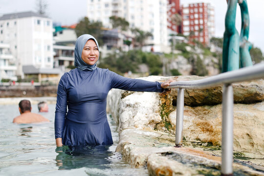 Filipina woman wearing light blue headscarf holding on metal railing inside the tidal pool
