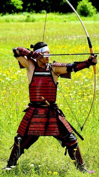 A skilled archer in traditional samurai armor draws back a bowstring amidst a vibrant meadow embodying strength precision and ancient Japanese warrior culture