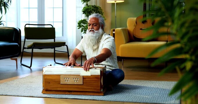Indian mid age stylish bearded man practicing vocals or singing at home, dedicated to daily riyaz while accompanying harmonium in modern home studio interior setting