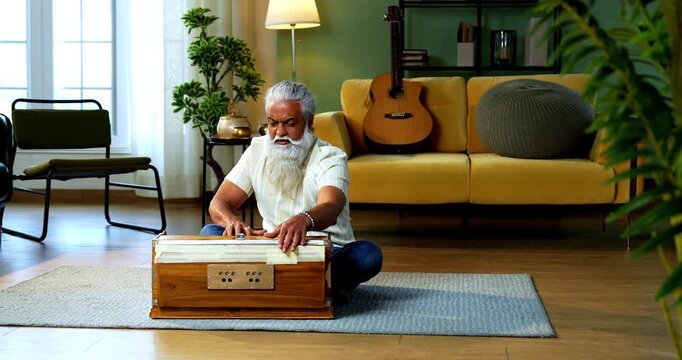 Indian mid age stylish bearded man practicing vocals or singing at home, dedicated to daily riyaz while accompanying harmonium in modern home studio interior setting