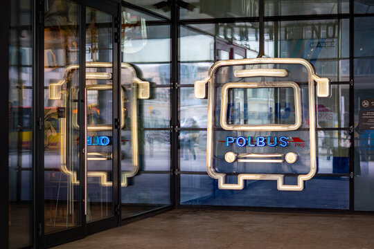Modern Polbus PKS neon sign shaped like a bus on a glass facade at Wroclaw station, stylish urban illumination, night architecture photography, public transport in Poland, glowing advertising sign.