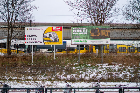 Outdoor advertising billboards for Lower Silesian Railways (Koleje Dolnośląskie) and DOLKOM near railway tracks, showcasing regional train connections and infrastructure recruitment in Poland.