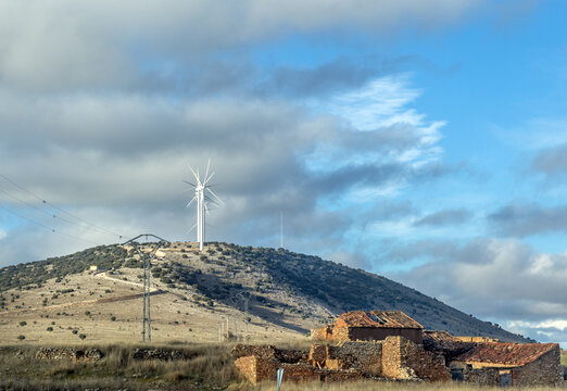 Modern wind turbines and deserted houses in the empty landscape of Soria province, Central Spain, on a partly overcast winter day
