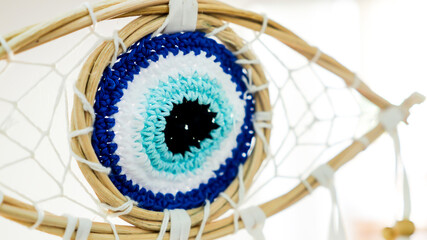 Crochet evil eye amulet integrated into a woven dreamcatcher, representing protection, spirituality, and good luck against negative energy and bad dreams with its intricate blue and white patterns