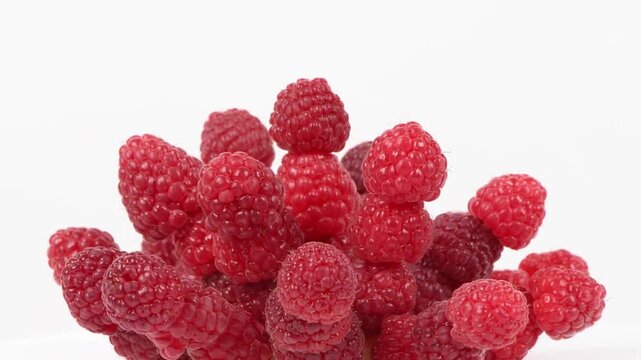 Abstract arrangement of fresh, ripe raspberries piled high against a clean white background.