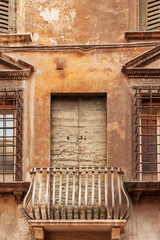 Obraz premium Historic medieval shabby building with metal balcony and wooden shutters in the narrow alley near Via Mazzanti, old town of Verona, Italy