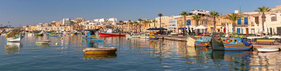 Colourful traditional luzzu boats are moored in the calm waters of Marsaxlokk harbour in Malta.