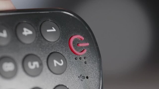 Close-up of Finger Pressing Red Power Button on Remote