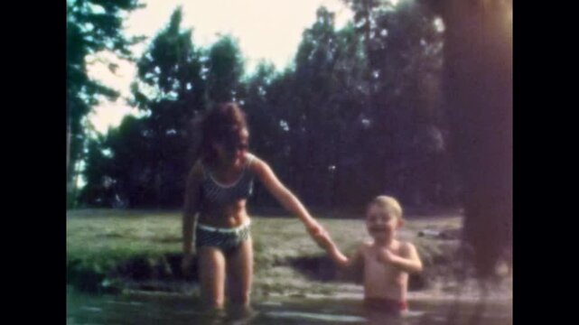 Mother tenderly holding her child hand as wades into lake waters on summer. Happy family outdoor recreation. Mother, toddler togetherness in river. Old film. Archival retro 1970s. Vintage archive
