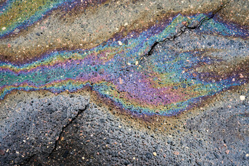 Oil spill on wet asphalt surface creating colorful iridescent patterns. Showing chemical pollution and abstract textures