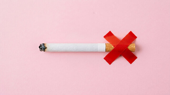 Single lit cigarette with a bright red ribbon crossed over the filter end symbolizing a definitive ban on smoking cessation against a soft pink background promoting health awareness.