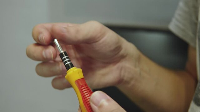 Male hand inserts metallic magnetized bit into manual screwdriver, closeup. Preparation of tip with miniature cross for work with small details.