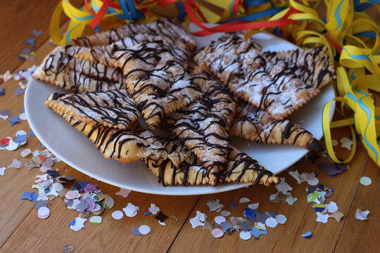 Italian sweet crisp pastry deep-fried and sprinkled with dark chocolate on wooden table with copy space. Chiacchere or crostoli, bugie, cenci with confetti and paper streamers