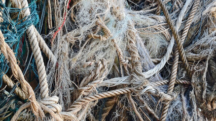 Tangled ropes and nets in a textured close-up, revealing the intricate details of nautical materials. Focus on the raw textures and subtle color variations of the worn and weathered materials
