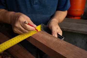 Primer plano de manos de carpintero marcando madera con lápiz y escuadra amarilla.