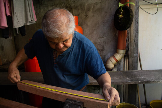 Carpintero de la tercera edad midiendo una viga de madera con una cinta m&eacute;trica en un taller r&uacute;stico.