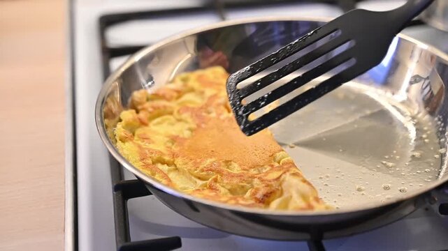 Cooking a fluffy omelet in a metal frying pan on a kitchen stove
