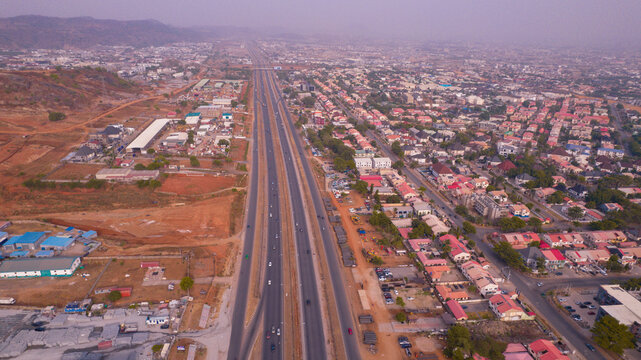 Aerial view of a long stretch of highway cutting through the urban landscape, juxtaposing the modern transport artery with the surrounding residential areas, Abuja, Federal Capital Territory, Nigeria.