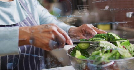 Slicing older Indian at kitchen counter with chef knife over bowl of greens, striped-apron blue-top © vectorfusionart