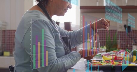 Slicing vegetables at kitchen counter, senior Indian cook in blue top dark apron with data overlay © vectorfusionart