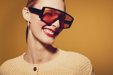 Smiling young woman with short hair wearing oversized orange sunglasses and a knitted beige...