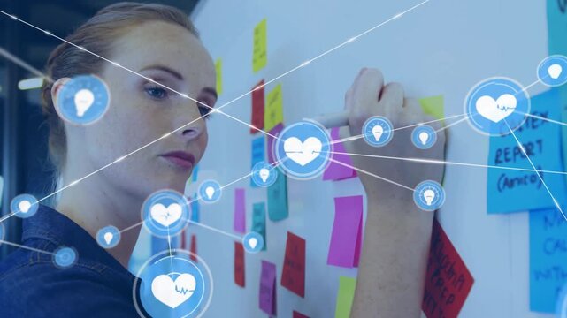 Woman writing on board, sorting notes and starting overlay icons growing around her for business