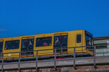 Gelber U-Bahnzug auf Hochgleisen vor blauem Himmel