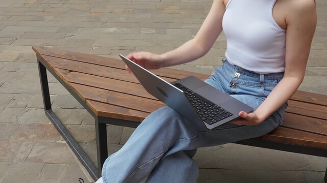 Person working on laptop while sitting on bench outdoors in urban area during daytime