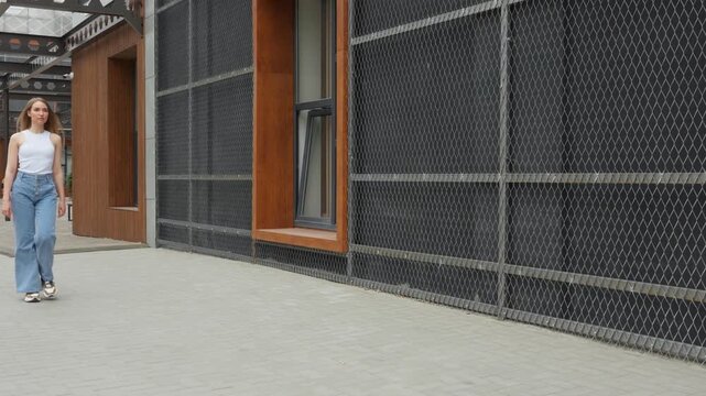 Young woman walks along a modern urban pathway near buildings made of metal and wood at noon