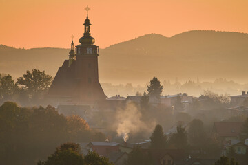 Wiejski kościół z wysoką wieżą we mgle w górskim krajobrazie w blasku wschodzącego słońca © piotr