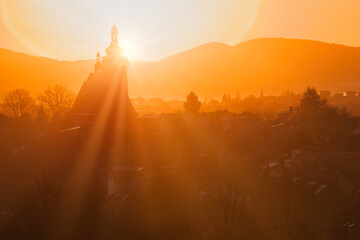 Wiejski kościół z wysoką wieżą we mgle w górskim krajobrazie w blasku wschodzącego słońca © piotr