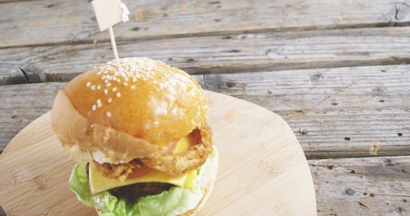 Stacked burger sitting on board at worn picnic table, with sesame bun, skewer flag, copy space © vectorfusionart