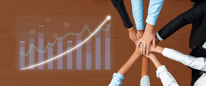 Hands of diverse team members stacked together on table display unity while a growth graph in background symbolizes collective effort towards success and progress. Axiom