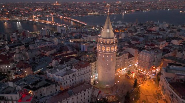 Morning view of Galata Tower illuminated against historic Golden Horn and cityscape in Istanbul with lights illuminating streets and buildings at sunrise. Flying around iconic Galata Tower in sunset.