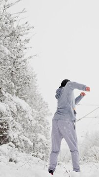 Man Leaps Over Snowbank Elegantly. Person Wearing Grey Tracksuit Leaps Above Snowy Terrain With Style. Male Athlete In Grey Tracksuit Executes Energetic Jump And Kick Above Snowlined Landscape