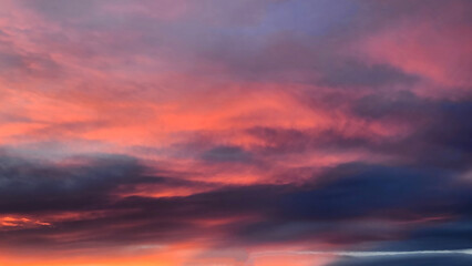 Obraz premium A dramatic winter glow in a cold February evening over the Mediterranean Sea. Deep crimson and fiery orange hues pierce through heavy, lilac clouds, reflecting the icy chill of the snowy peaks nearby.