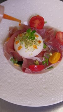 Close up of fresh burrata cheese salad preparation process. Unrecognizable chef of italian restaurant preparing for serving starter from seasonal menu. High quality FullHD footage