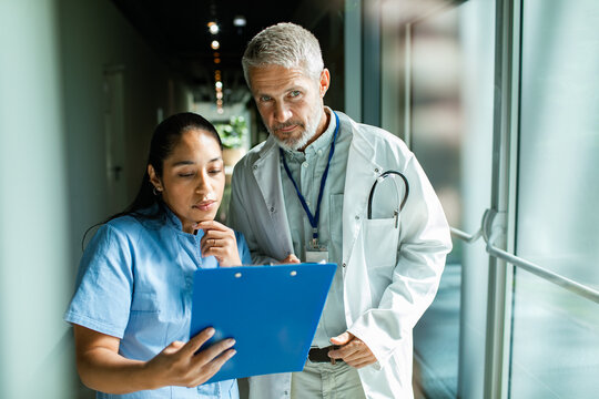 Doctor and nurse reviewing patient chart in hospital corridor