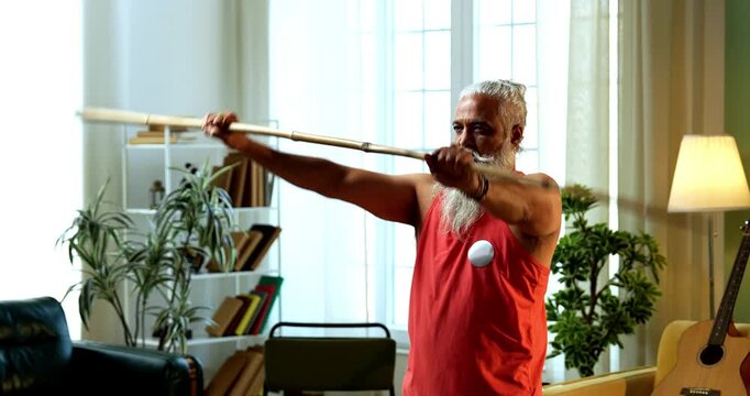 Indian mid age stylish bearded man doing exercise using stick, rod or staff at home, fitness conscious mature male performing strength and mobility workout showing agility and determination